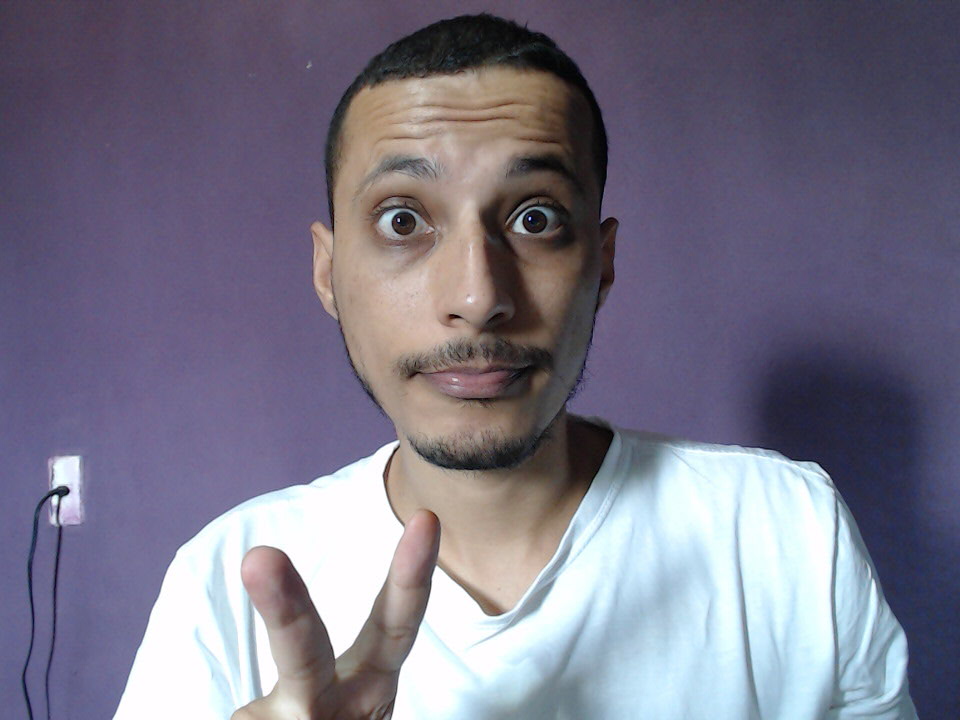 foto do Maires peace and love, olhos arregalhados fazendo bico, camisa branca,fundo roxo